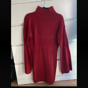 Röd stickad poloklänning - Mysig röd stickad klänning med polokrage och långa ärmar. Klänningen har en rak passform och är perfekt för kyligare dagar. Ribbstickad struktur ger en snygg detalj och extra komfort.