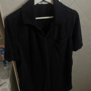 Mörkblå frotté skjorta John Henric - Mörkblå skjorta från John Henric i mjuk frotté. Klassisk krage, korta ärmar och bröstficka ger en chill och stilren vibe. Perfekt till jeans eller shorts för en avslappnad look.