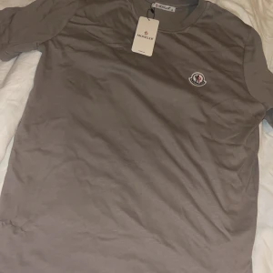 Beige t-shirt från Moncler,  - Snygg beige t-shirt från Moncler med klassisk rund hals och korta ärmar. T-shirten har Moncler-logga broderad på bröstet och är tillverkad i mjuk 100% bomull. Perfekt för dig som gillar stilrena och exklusiva plagg.