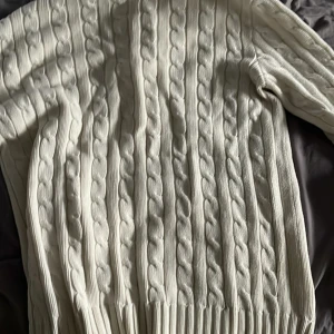 Vit kabelstickad tröja från Ralph Lauren - Säljer en vit kabelstickad tröja från Ralph Lauren med klassisk rund hals och långärmad design. Tröjan har det ikoniska Polo-logot broderat på bröstet och är tillverkad i mjuk bomull. Perfekt för dig som gillar preppy stil och vill ha något snyggt och bekvämt.