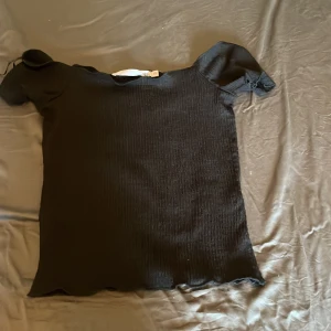 Svart ribbad topp från 157, XS - Säljer en svart ribbad topp från 157 i storlek XS. Toppen har korta ärmar och en lätt stretchig struktur med diskret vågig kant nertill. Enkel och stilren modell som passar till många olika looks.