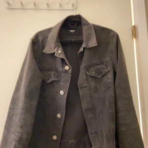 Svart/grå  jeansjacka från Bik Bok XS - Säljer en svart jeansjacka från Bik Bok i storlek xs, silverfärgade knappar och två bröstfickor med lock.. Enkel att styla till olika outfits. Har knappt användt den för inte min stil annars väldigt snygg!