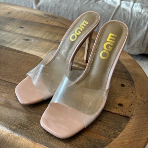 EGO klackar med transparent rem - Snygga klackar från EGO i ljusrosa med transparent rem över foten. Skorna har öppen tå, hög klack och fyrkantig tåform. Tillverkade i syntetmaterial och perfekta för dig som vill sticka ut med en modern look.