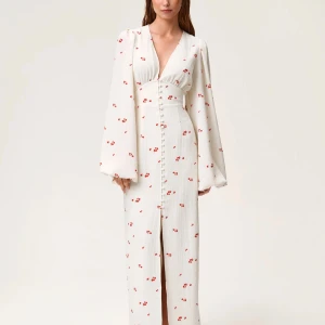 Adoore klänning  - Superfin långklänning från Adoore i  creme färg med små röda blommor. Djup v-ringning, markerad midja och långa puffärmar. Klänningen har klädda knappar framtill och en liten slits. Perfekt för sommarens speciella tillfällen!🌼