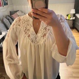 Vit blus med spets från Bik Bok - Supersöt vit blus från Bik Bok i storlek XS. Blusen har v-ringning, transparent spets upptill och vida, långa ärmar.