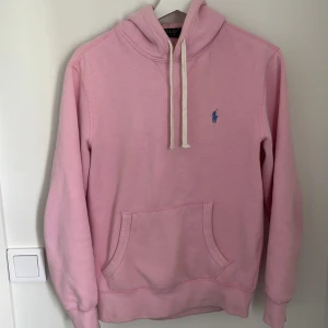 Rosa hoodie från Polo Ralph Lauren XS - Säljer en ljusrosa hoodie från Polo Ralph Lauren i storlek XS. Tröjan har huva med vita snören, känguruficka och blå broderad logga på bröstet. Mjuk bomullskvalitet och klassisk passform, perfekt för chill dagar.