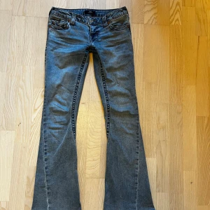 True Religion Joey Low Rise Flare Jeans - Snygga blå jeans från True Religion, modell Joey Low Rise Flare. Låg midja och utsvängda ben ger en cool retrovibe. Klassiska fickor med lock och knappar bak, samt detaljerade sömmar. Perfekta för dig som gillar statement-jeans med unik passform.