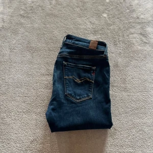 Blå Replay jeans, midwaist, W27 L30 - Snygga blå jeans från Replay med klassisk femficksdesign, kontrastsömmar och läderpatch bak i midjan. Jeansen har en rak passform och är tillverkade i mjukt denimtyg med diskret tvättad look. Perfekta för dig som gillar stilrena och tidlösa jeans.