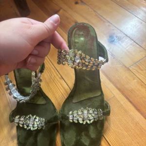 Gröna sammetsandaler med strass - Snygga sandaler i mörkgrön sammet med hög klack och dekorerade med glittrande strassdetaljer på remmarna. Skorna har öppen tå och en elegant, smal klack som ger en riktigt chic vibe. Perfekta för dig som vill sticka ut med något unikt och glam. Made in italy.    Priset+frakt