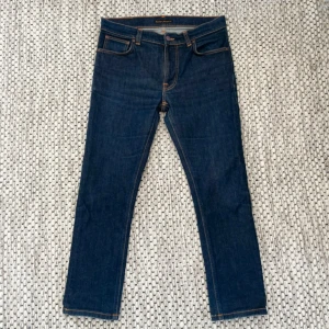 Nudie Jeans  - Mörkblå jeans från Nudie Jeans med klassisk femficksdesign och kontrastsömmar. Snygga bakfickor med Nudie-signatur och patch i läder.  Dem är som nya. Är tillverkad i slitstark bomullsdenim. 33/30