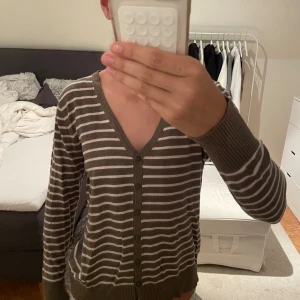 Randig kofta från Gina Benotti - Mysig brun och beige randig kofta från Gina Benotti med v-ringning och knappar framtill. Långärmad modell med ribbade muddar och nederkant. Perfekt för lager-på-lager och enkel att matcha med jeans eller kjol.