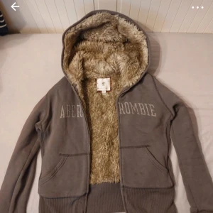Brun hoodie från Abercrombie med fuskpäls - Mysig grå hoodie från Abercrombie med fluffigt fuskpälsfoder i hela insidan och huva. Tröjan har dragkedja framtill, två fickor och broderad logga över bröstet. Perfekt för kyliga dagar och riktigt skön att ha på sig. Vintage! Passar som typ xs/s men skulle säkert passa m också! ‼️inte mina bilder‼️