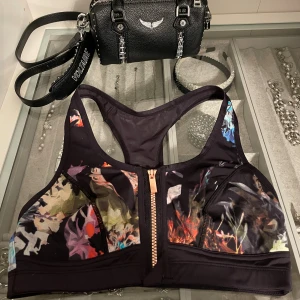 Blommig sporttopp - Sporttopp i svart med färgglatt blommönster och snygg dragkedja framtill. Perfekt för träning. Aldrig använd.