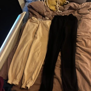 Beiga och svarta mjukisbyxor - Två par mjukisbyxor i klassisk modell med resår i midjan och vid bensluten. Ena paret är beige och det andra är svart, båda i mjukt bomullsmaterial. Perfekta för chill dagar eller när du vill vara extra bekväm.    Båda två kostar tillsammans 50kr