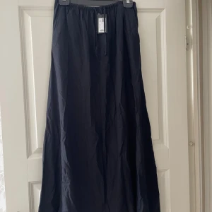 Svart långkjol i bomull - Enkel och stilren svart långkjol i mjuk bomull. Kjolen har resår i midjan med dragsko för skön passform och ett flowy fall. Perfekt att styla med sneakers eller sandaler för en chill look.