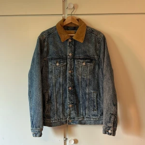 Jeansjacka med manchesterkrage Pull&Bear - Säljer en snygg blå jeansjacka från Pull&Bear med ljusbrun manchesterkrage. Jackan har klassiska knappar framtill och två bröstfickor. Perfekt för dig som gillar retrovibbar och vill ha en unik detalj i garderoben.