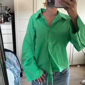 Grön skjorta från co'couture - Snygg grön skjorta från co'couture med oversized passform och långa, vida ärmar. Skjortan har klassisk krage, knappar framtill och en cool knytning vid midjan. Perfekt att styla med jeans för en trendig look.