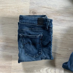 Mörkblå jeans med klassisk passform - Säljer ett par mörkblå jeans med klassisk femficksdesign och snygga slitningar. Jeansen har normal midja och raka ben, perfekt för en avslappnad stil. Materialet är robust denim och de har detaljerade sömmar på bakfickan.