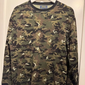 Camouflage långärmad tröja Polo Ralph Lauren - Säljer en långärmad tröja från Polo Ralph Lauren i klassiskt camouflage-mönster. Tröjan är i 100% bomull med broderad logga på bröstet. Färgerna går i grönt, brunt, svart och beige. 