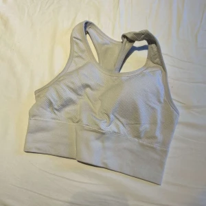 Ljusgrå ribbad linnetopp - Säljer en ljusgrå ribbad linnetopp med brottarrygg. Toppen är ärmlös och har bred resår nedtill för extra stöd. Perfekt för träning eller chill dagar. Materialet är mjukt och stretchigt syntet, vilket gör den riktigt bekväm att bära.