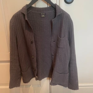 Grå kofta från Massimo Dutti i bomull - Storlek L men passar M. Säljer en grå kofta från Massimo Dutti i 100% bomull. Koftan har ett vågigt stickat mönster, knappar framtill, två fickor och lång ärm. Perfekt för lager-på-lager och chill stil.
