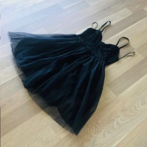 Svart spetsklänning med tyllkjol - Supersöt svart kortklänning med smala axelband, blommig spets upptill och fluffig tyllkjol. Perfekt för dig som vill ha en feminin och trendig look. Klänningen har figurnära överdel och voluminös kjol som ger en snygg siluett. Helt ny!