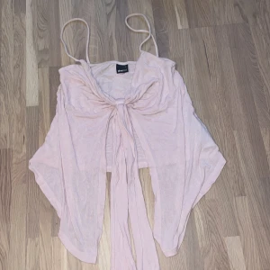Ljusrosa omlottopp från Gina Tricot - Supersöt ljusrosa omlottopp från Gina Tricot med tunna axelband och knyt framtill. Toppen är croppad och har en flowy passform som ger en avslappnad vibe. Perfekt för varma dagar och snygg att styla med jeans eller kjol.