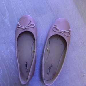 Ljusrosa ballerinaskor med rosett från Alley - Söta ballerinaskor i ljusrosa från Alley med rund tå och dekorativ rosett framtill. Skorna har en klassisk och enkel design med platt sula och mjukt syntetmaterial. Perfekta för dig som gillar en stilren och feminin look. skorna har storlek 36 men passar även mig som har 37/38