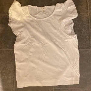 Vit blus med spetsdetaljer från H&M - Säljer en söt vit blus från H&M med korta ärmar och fina spetsdetaljer. 