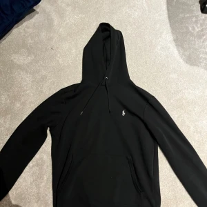 Svart hoodie från Polo Ralph Lauren - Svart hoodie från Polo Ralph Lauren storlek S, passar cirka 170 cm mer eller mindre, använd ganska mycket som dock inte syns, förutom att en av metallgrejen på en av trådarna till luvan åkt av. Hör av er om minsta fundering💫