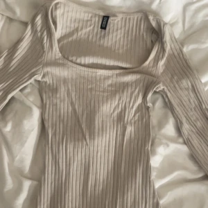 Beige ribbad klänning från Divided - Supersnygg beige ribbad klänning från Divided i storlek XXS. Klänningen har lång ärm, rundad fyrkantig urringning och är figurnära (tightare vid midja). Perfekt för dig som gillar enkel men trendig stil.