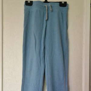Ljusblå mjukisbyxor från Vossatassar - Ljusblå mjukisbyxor från Vossatassar med ribbad midja, grå snörning och resår vid bensluten. Perfekta för chill dagar. Klassisk passform och enkel stil som funkar till det mesta. Byxorna är noppriga.
