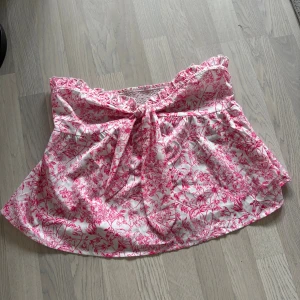 Vit och rosa blommig topp med knyt - Supersöt topp i vitt med rosa blommigt mönster toppen har en fin knyt-detalj framtill och är gjord i mjuk polyester som känns lätt och luftig. Perfekt för dig som gillar romantiska och färgglada plagg! Oanvänd endast testad 