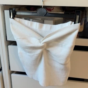 Vit stickad tubtopp med knutdetalj - Supersöt vit stickad tubtopp med en snygg knutdetalj framtill. Toppen är ribbstickad och har en tight passform och perfekt för dig som vill ha en trendig och stilren look med det lilla extra.