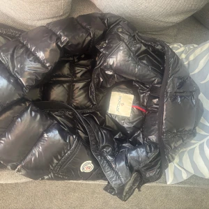 Svart dunjacka från Moncler med bälte - Svart dunjacka från Moncler och markerad midja tack vare bältet. Jackan har dragkedja framtill, fickor med tryckknappar och Moncler logga på ärmen. Jackan är äkta men har inte mina äkthetsbevis kvar men man ser på jackan att den är äkta. 