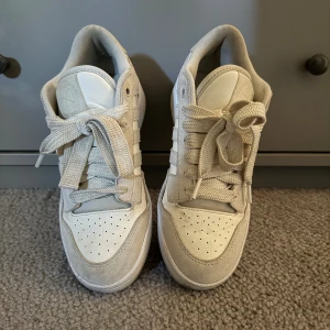 Vita adidas sneakers med mockadetaljer - Säljer ett par stilrena vita adidas sneakers med klassiska tre ränder på sidan. Skorna har snörning, rund tå och detaljer i mocka och skinn. Perfekta för dig som gillar en clean look och vill ha bekväma skor till vardags. Adidas-logga på plösen och sulan. Köpta för 650 