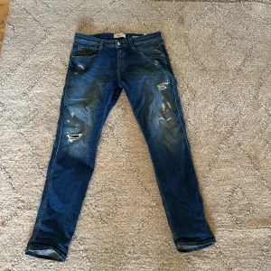 Replay Anbass blå slitna jeans - Snygga blå jeans från Replay, modell Anbass, med slim fit och slitna detaljer på benen. Klassisk femficksdesign, normal midja och läderpatch bak i midjan. Perfekta för dig som gillar en trendig och avslappnad look. Helt nya, nästan aldrig använda, as bra skick på dem, nypris 1899, mitt pris 1299. Storlek 34, 34. Säljer dom då dom är för stora för mig. Såklart inga defekter eller skador!