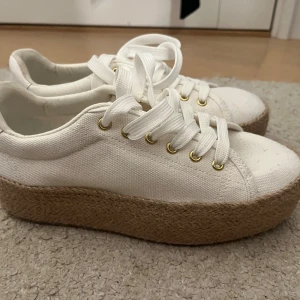 Vita sneakers, flätad sula - Ej använda, om använda max 2ggr. Snygga vita sneakers i canvas med breda vita snören och guldfärgade öljetter. Skorna har en platåsula i fläta som ger extra höjd. 