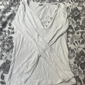 Vit ribbad långärmad tröja med knappar - Vit långärmad tröja från Cubus i ribbad bomull med djup v-ringning och tre små knappar framtill. Enkel och stilren modell som passar perfekt till jeans eller kjol. Snygg basic för garderoben.