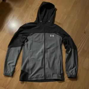 Under Armour Jacka S - Under armour jacka I storlek S, grå. Enda defekterna är att det är svårt att stänga jackan eftersom dragkedjan är lite förstörd alltså svårt att stänga jackan därav priset 