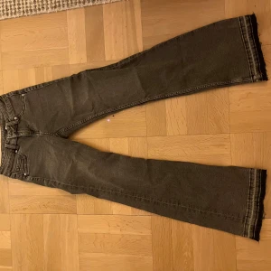 Mörkgrå bootcut jeans med rå kant - Snygga mörkgrå jeans med bootcut passform och rå, fransig kant längst ner på benen. Klassisk femficksmodell med dragkedja och knapp. Perfekta för dig som gillar en avslappnad men trendig stil.