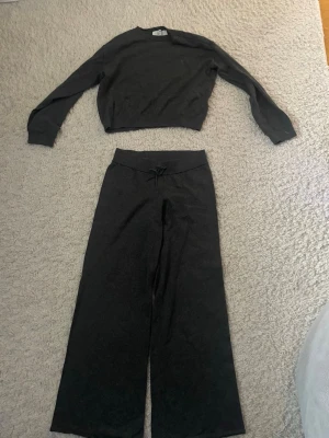 Mörkgrått loungewear-set från H&M - Mysigt tvådelat loungewear-set från H&M i mörkgrå färg. Setet består av en långärmad tröja med rund hals och ett par vida byxor med dragsko i midjan. Perfekt för chill dagar hemma eller när du vill vara bekväm. Materialet är mjukt och stretchigt.