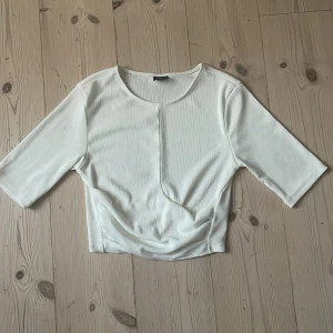 Vit croppad topp från Gina Tricot - Säljer en vit croppad topp från Gina Tricot. Toppen har rund halsringning, halvlånga ärmar och är tillverkad i ett ribbat material och går lite om lått längst ner. Helt oanvänd och bra passform.