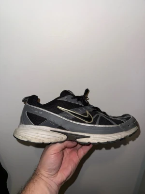 Nike svart/grå sneakers med snörning - Säljer ett par snygga Nike sneakers i svart och grått med klassisk vit sula och metallic silver swoosh. Skorna har meshpaneler för bra ventilation och coola detaljer längs sidorna. Perfekta för dig som gillar sportig stil och vill ha något bekvämt till vardags.