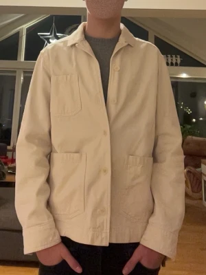 Beige overshirt från these glory days - Stilren beige overshirt från Norse Projects med tre utanpåliggande fickor och klassisk krage. Tillverkad i kraftig bomullsväv och stängs med knappar framtill. Perfekt lager-på-lager-plagg för en avslappnad look.