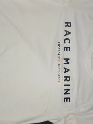 Vit Race Marine t-shirt i bomull - Snygg vit t-shirt från Race Marine med tryck i marinblått och röda detaljer på bröstet. Klassisk rund halsringning och korta ärmar. Tillverkad i mjuk bomull som känns skön mot huden. Pris kan diskuteras