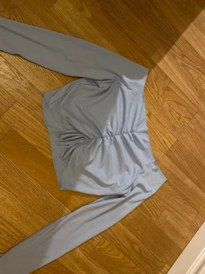 Ljusblå långärmad topp med rynk - Trendig ljusblå långärmad topp med rynkdetalj framtill och smal passform. Tillverkad i ett mjukt, stretchigt material som känns bekvämt mot huden. Perfekt att styla med jeans eller kjol för en snygg look.