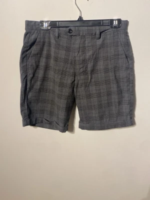 Grå rutiga shorts med fickor - Snygga grå shorts med rutig design och klassisk passform. Shortsen har framfickor, bälteshällor och knäppning fram. Perfekta för en stilren look under varmare dagar.