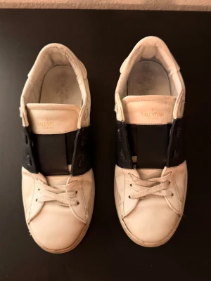Valentino Open - Snygga Valentino Open sneakers i färg vit med svart band. Märkeslogga på plösen i guld. Skorna är använda men fortfarande i bra skick. Priset går att diskutera.