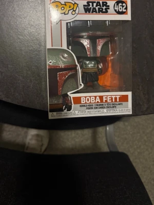Funko Pop! Boba Fett Star Wars - Säljer en Funko Pop! figur av Boba Fett från Star Wars-serien Mandalorian. Figuren är nummer 462 och kommer i originalförpackning. Färgerna är röd, grön och svart med detaljer i silver. Perfekt för samlare eller Star Wars-fans.